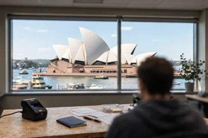 Sydney Opera House seen through a visa centre window, with a passport and fingerprint scanner on the desk.