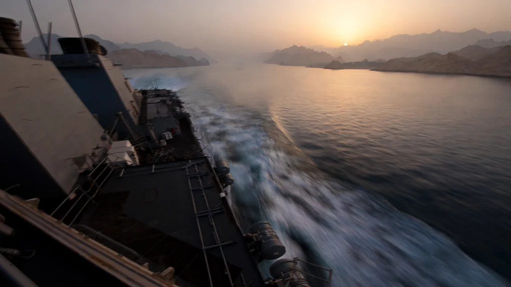 A vessel transits the Strait of Hormuz at sunrise. Photo: US Navy via Wikimedia Commons (background composite).