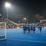 India field hockey players in blue celebrate under floodlights on a blue turf pitch in Jalandhar.