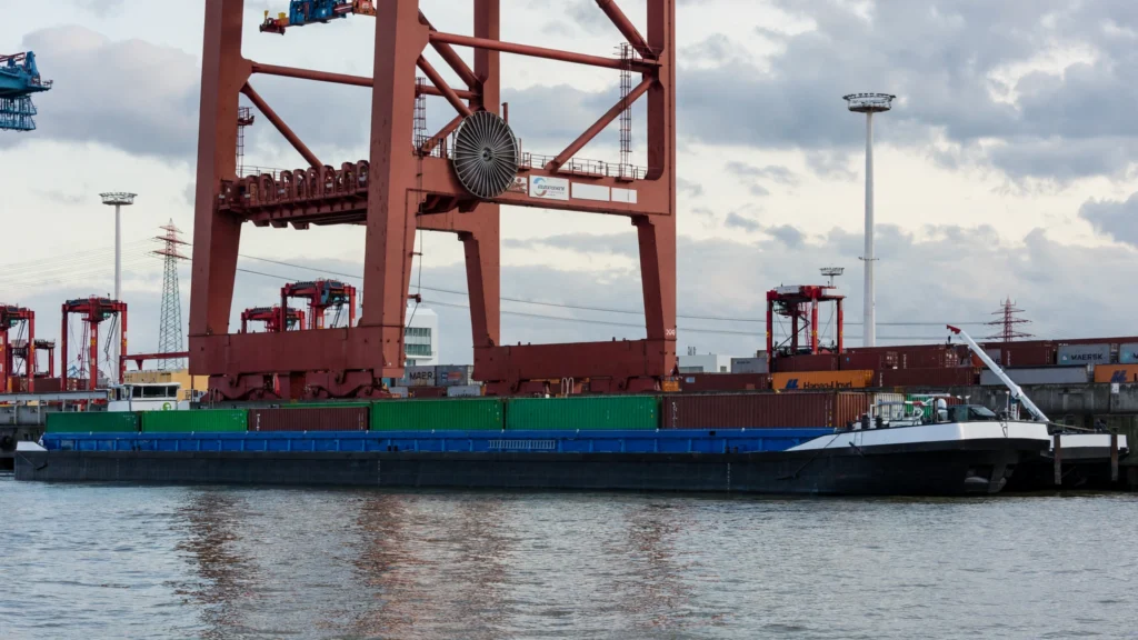 Container barge at a cargo terminal with cranes. Image generated from a real Wikimedia Commons reference photo.