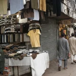 Busy Indian bazaar street with clothing stalls and shoppers, illustrative image grounded in a real Chandni Chowk market photo