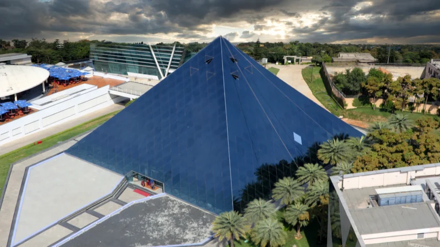 The glass pyramid of the Infosys campus in Bengaluru. Photo: Vinu Thomas / Wikimedia Commons (CC BY-SA 2.0), background composite.