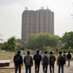 JNU library tower on campus, students walking towards it. AI-generated image grounded in a real Wikimedia Commons photo of the JNU library building.