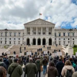 Crowd outside Portugal's parliament in Lisbon during the October 27 housing protest. AI-generated image grounded in a real photo of the Palacio de Sao Bento (Einaz80, Wikimedia Commons, CC BY-SA 4.0).
