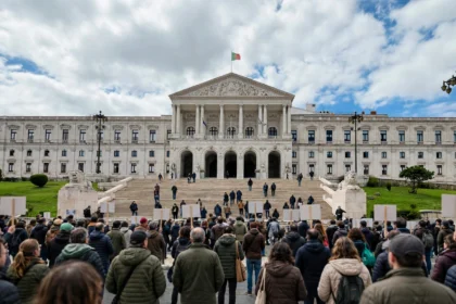 Crowd outside Portugal's parliament in Lisbon during the October 27 housing protest. AI-generated image grounded in a real photo of the Palacio de Sao Bento (Einaz80, Wikimedia Commons, CC BY-SA 4.0).