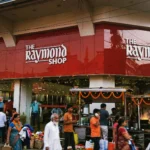 The Raymond Shop storefront in Kolkata, with shoppers outside during the festive season. Photo: Innocentbunny / Wikimedia Commons, CC BY-SA 3.0 (background composite)