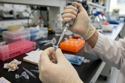 A researcher in a biotechnology laboratory using a pipette with micro test tubes. AI image grounded in a real public-domain laboratory photo by Maggie Bartlett, NHGRI.