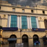 State Bank of India branch building with blue SBI signage. Photo: Pinakpani / Wikimedia Commons, CC BY-SA 4.0 (editorial background composite).