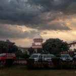 Supreme Court of India building at dusk. Photo: Pinakpani / Wikimedia Commons (CC BY-SA 4.0), editorial composite.