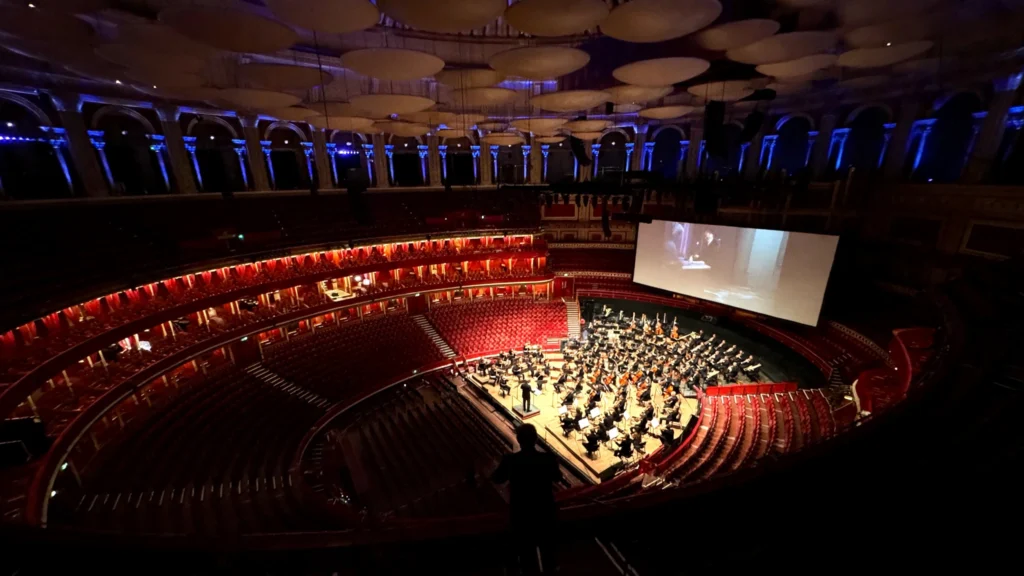 Orchestra on stage below a cinema screen in a grand concert hall