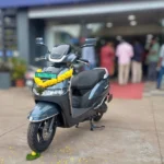 TVS iQube electric scooter outside a dealership in India. AI image grounded in a real photo by Maneesh Sreekariyam, CC BY-SA 4.0, via Wikimedia Commons.